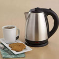 Stainless steel kettle with a cup of tea and cookies on a beige background